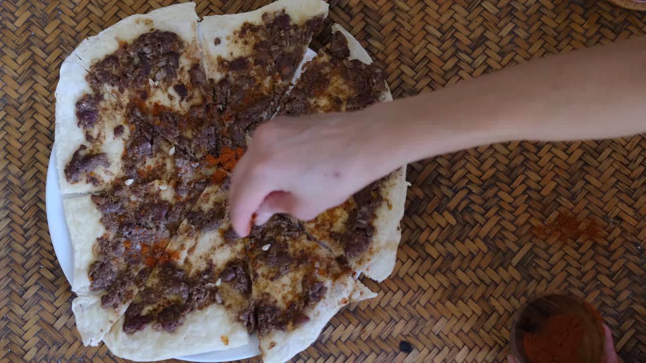 cerca de una mano poniendo especias en manakish lahm bi ajeen - panes planos con cordero picado o carne de res y pastel relleno de fatayer con espinaca. comida árabe tradicional