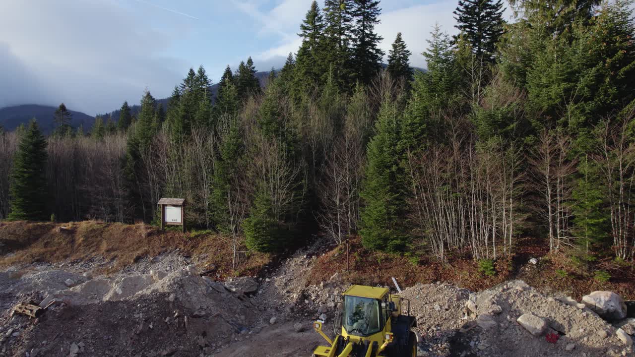 volando sobre una excavadora en un sitio de construcción que muestra hermosos bosques y montañas vírgenes