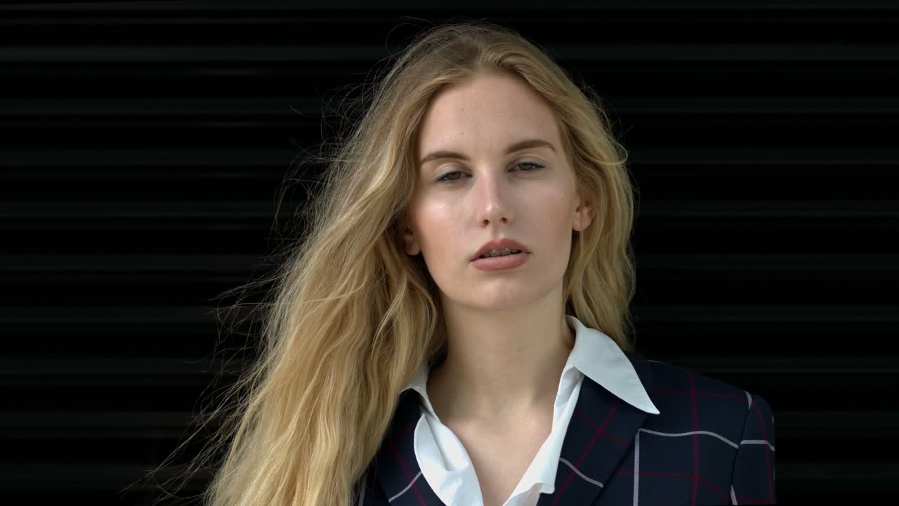 느린 동작으로 검은색 배경에서 매력적인 젊은 금발 여성이 카메라를 마주하고 자신 있게 직접 응시합니다.
