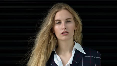 in slow motion, on a black backdrop, an attractive young blonde women faces the camera and gazes directly and with confidence