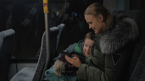 Child-and-mother-traveling-by-bus-and-looking-at-photos-in-cellphone