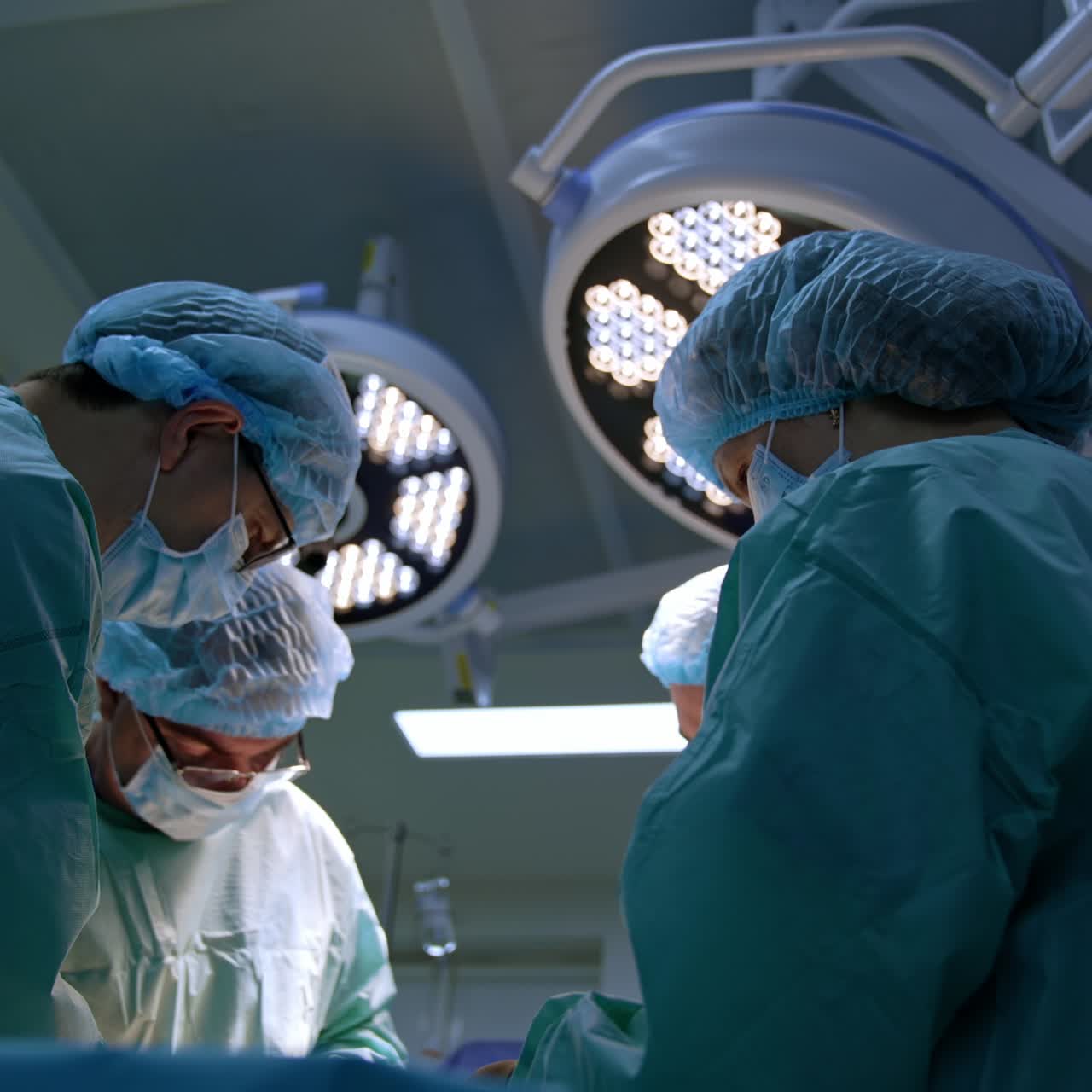 Group of surgeons and nurse stand around the patient on the operational table. Male chief surgeon uses a mallet. Low angle view