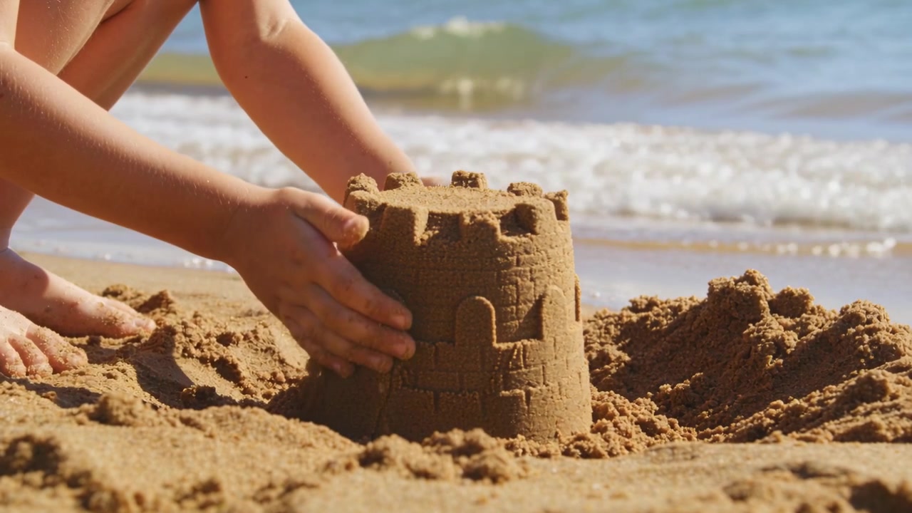Lyfter formen, barn i badkläder som färdigställer sandslott på stranden, stabiliserar med händerna innan vågorna