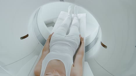 paciente femenina acostada en una tomografía computarizada o resonancia magnética, la cama se mueve dentro de la máquina escaneando su cuerpo y cerebro. en un laboratorio médico con equipos de alta tecnología. toma de cámara elevada.