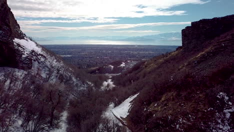 Flying-between-two-cliffs-to-see-the-city-in-the-valley-below-with-mountains-and-a-huge-lake-beyond