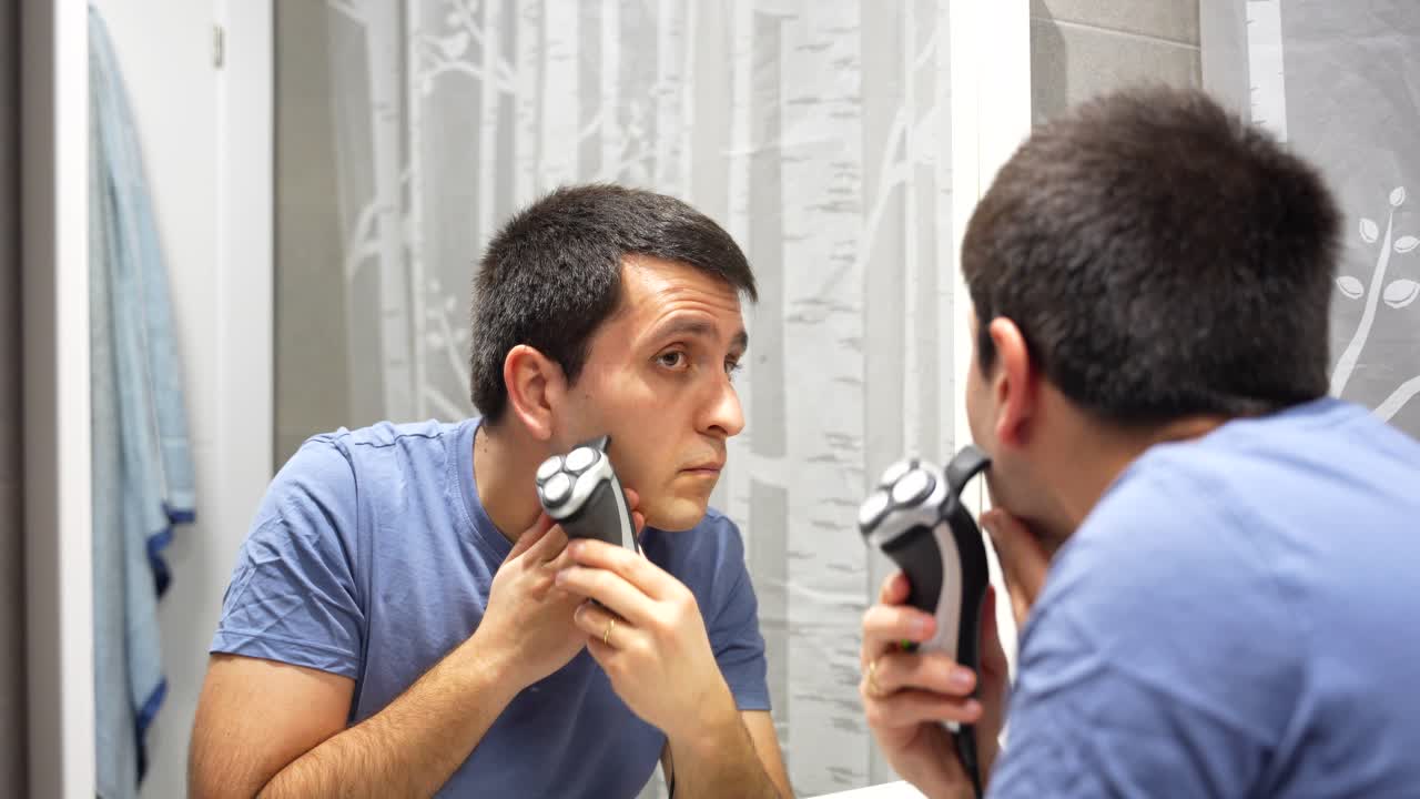 Primo piano di un uomo che si taglia le basette con un rasoio elettrico, zoom indietro