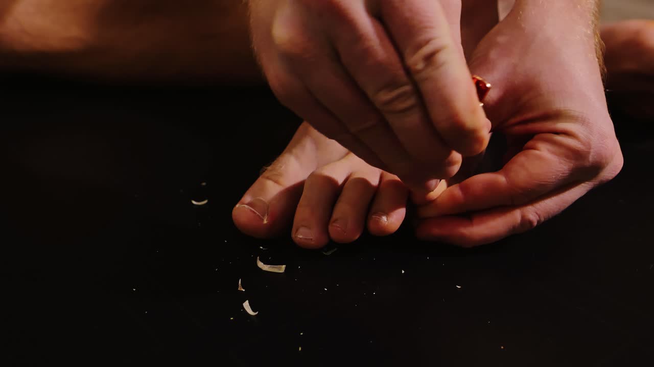 Man uses bronze nail clippers on little toe in low light with dark background