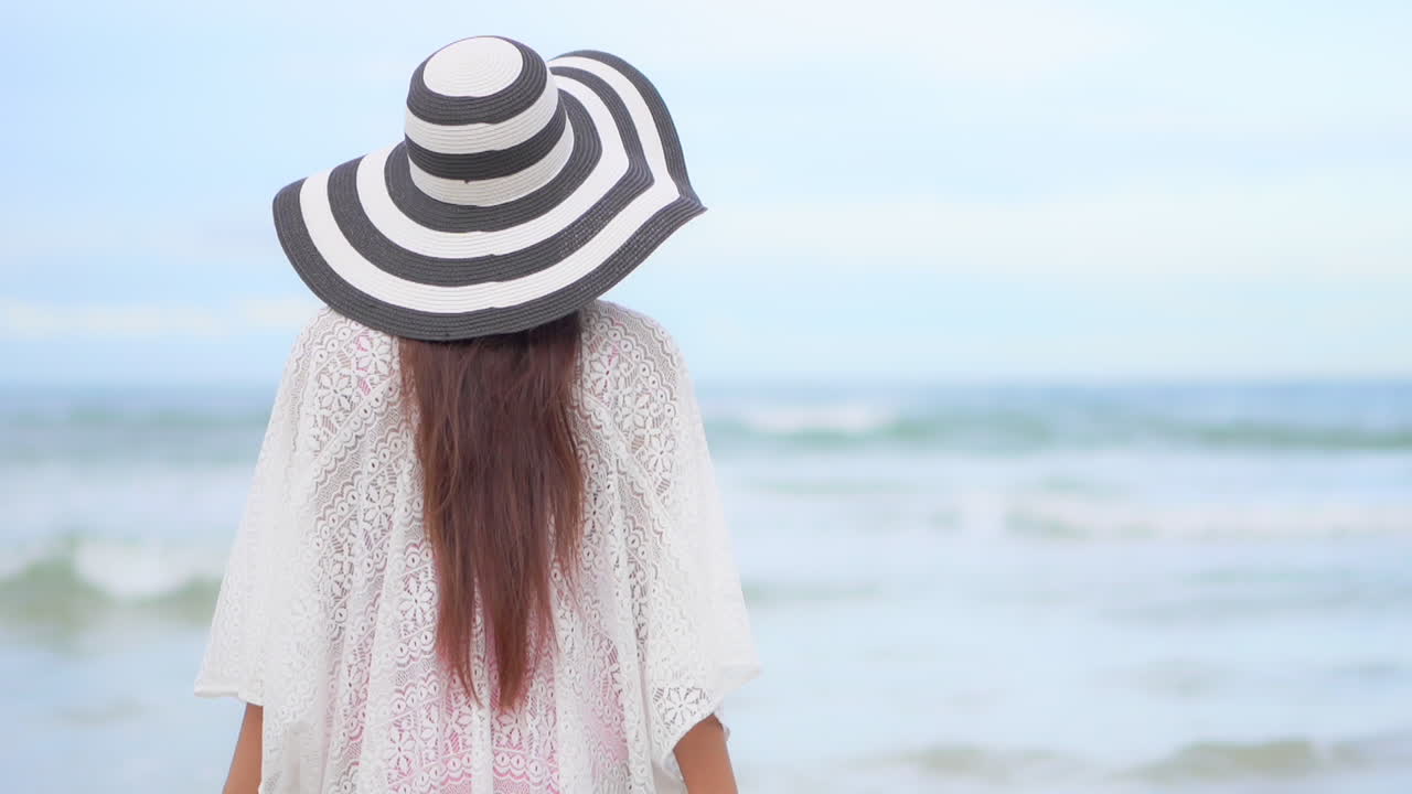 흰색 선드레스를 입은 알아볼 수 없는 여성 여행자와 해안가를 바라보는 모자를 벗은 여성 여행자
