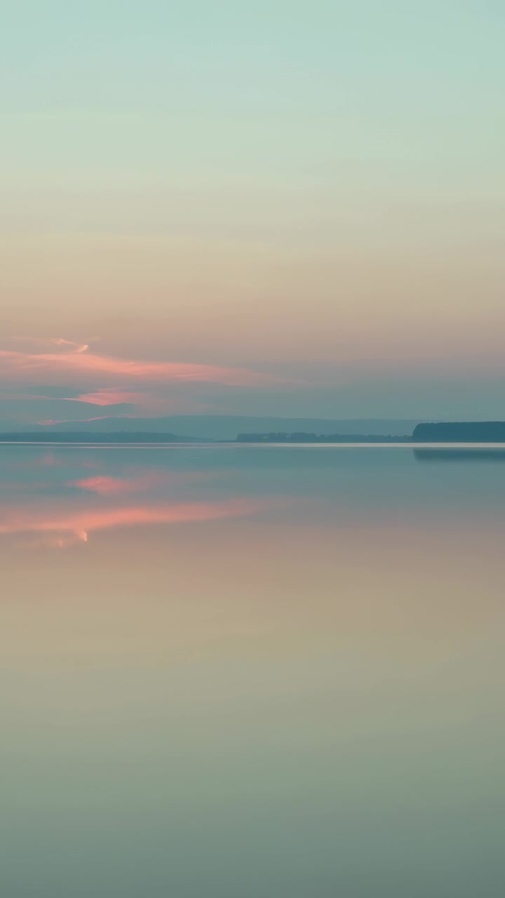 Vertical video: Showing calm water reflecting pastel clouds at bay, light shifting on right cliff