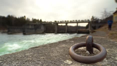 watching the flowing water coming through a weir while a unfocused man is walking in direction of the camera