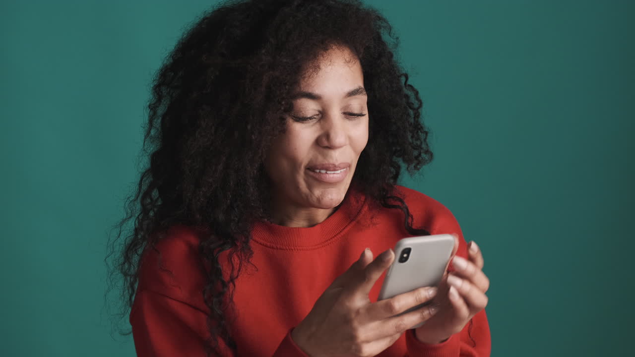 African american smiling woman using smartphone over blue background.