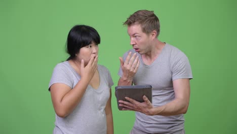young multi-ethnic couple using digital tablet and looking shocked together