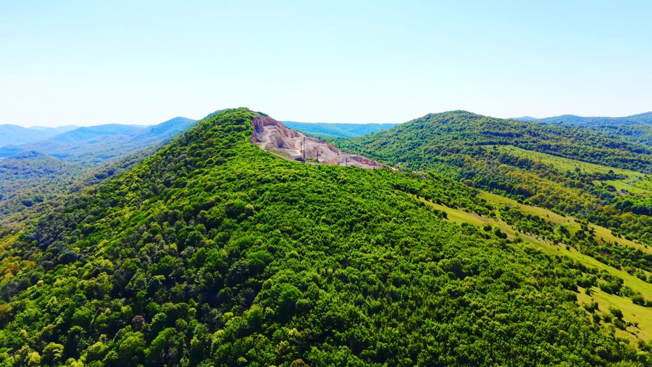 Cava di roccia in cima a una collina in una foresta, Bulgaria. Ripresa da drone di un sito di scavo industriale sulla cima di una montagna circondato da fitta boscaglia e terreno ondulato.