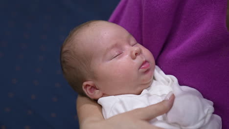 caring mother is holding baby and shaking her child tenderly. baby boy sleeping sweetly in mommy's hands. mom stroking baby cheek with her finger.