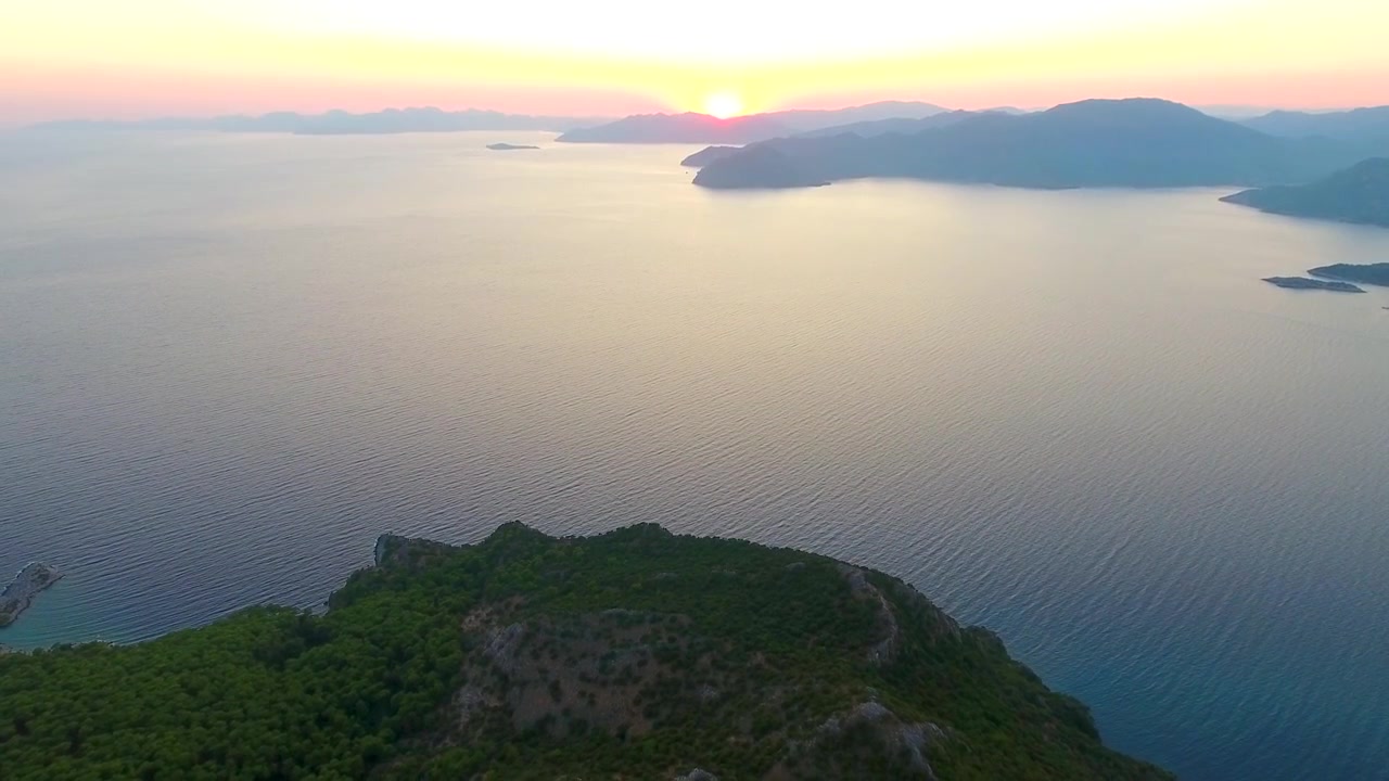Luftfoto af en kystnær bjergpeninsula ved solnedgang