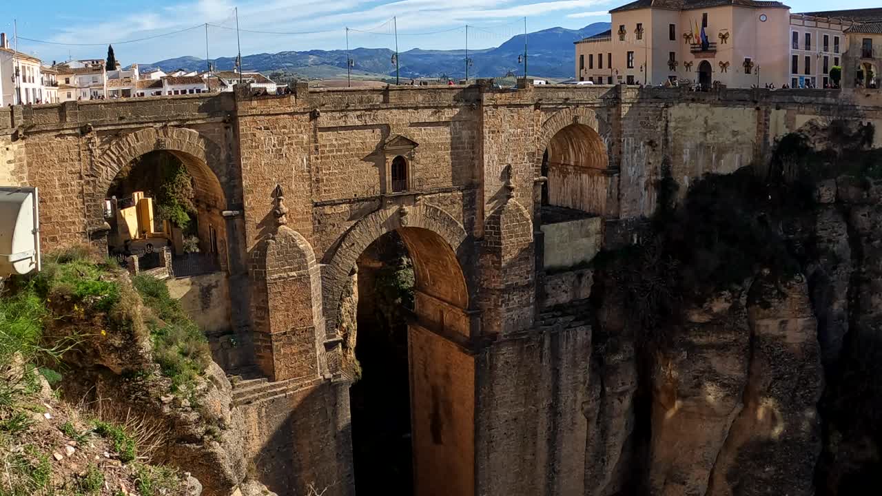 Handheld tilt up reveals ronda bridge built of red brick on sunny day