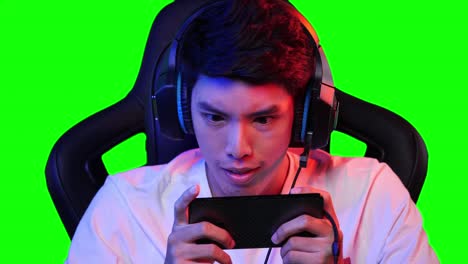 esports gamer hombre jugando juegos en línea en el teléfono inteligente en casa. hombre asiático controlando la consola con teléfono inteligente en el videojuego. joven juego de ocio en la sala de estudio y pantalla verde en casa.