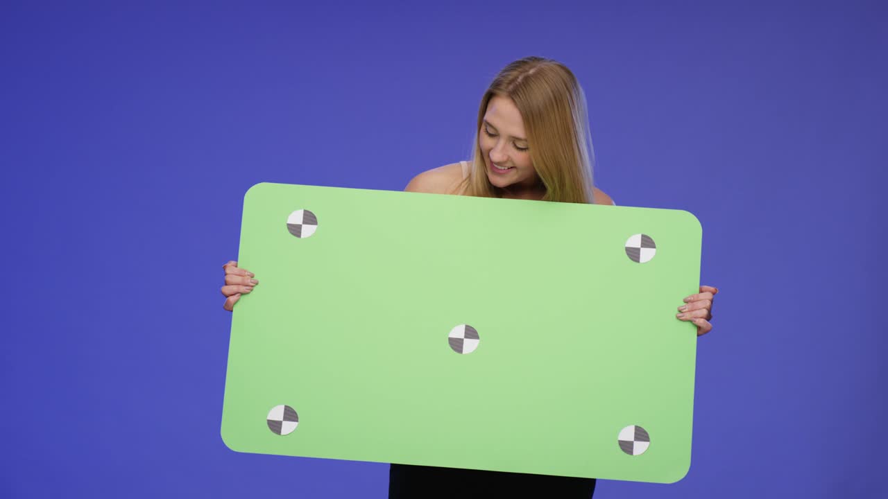 impresionante mujer hermosa sosteniendo una tarjeta en blanco de gran tamaño con fondo de pantalla azul