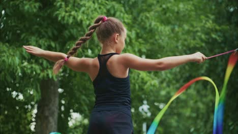 a young girl showcases her rhythmic gymnastics skills in a lush green setting, gracefully manipulating colorful ribbons with elegance and precision as she performs