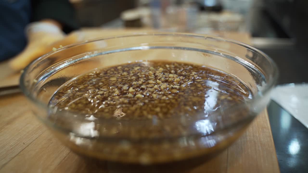 Minced garlic and is being transported by a sharp knife to a small clear glass bowl.