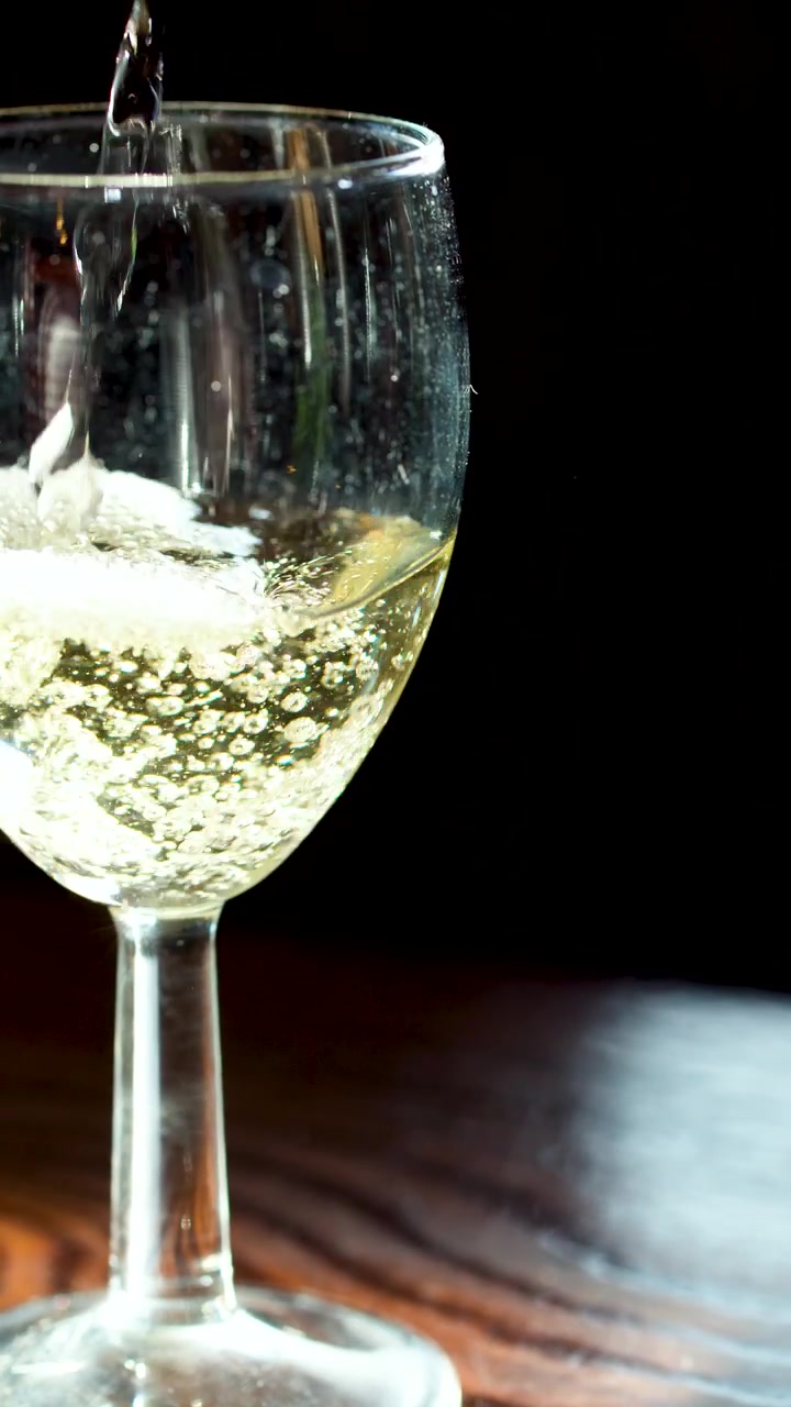 Bevanda frizzante versata in un calice di vino trasparente, bollicine che salgono, illuminazione laterale, sfondo scuro, inquadratura statica
