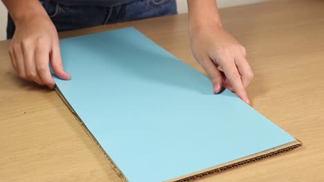 hands methodically fold blue paper on a wooden table under soft lighting, demonstrating a step-by-step process
