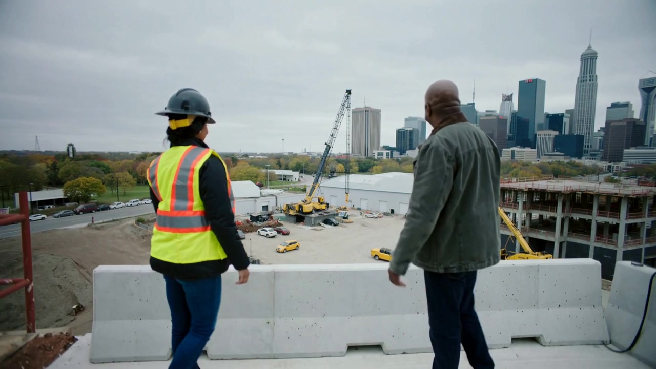 Pointing supervisor guiding inspector in hard hat and vest at rooftop barrier, inspecting site