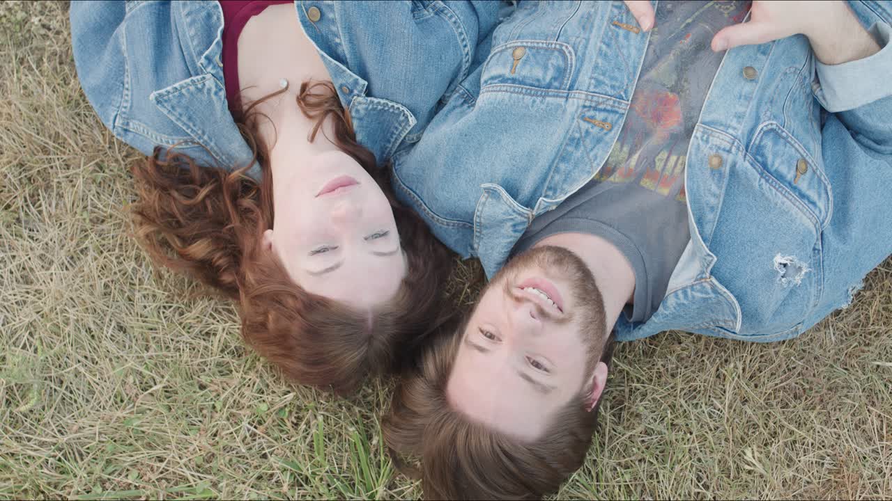 Couple point to the sky while laying together on the grass outdorrs in a park