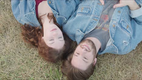 couple point to the sky while laying together on the grass outdorrs in a park