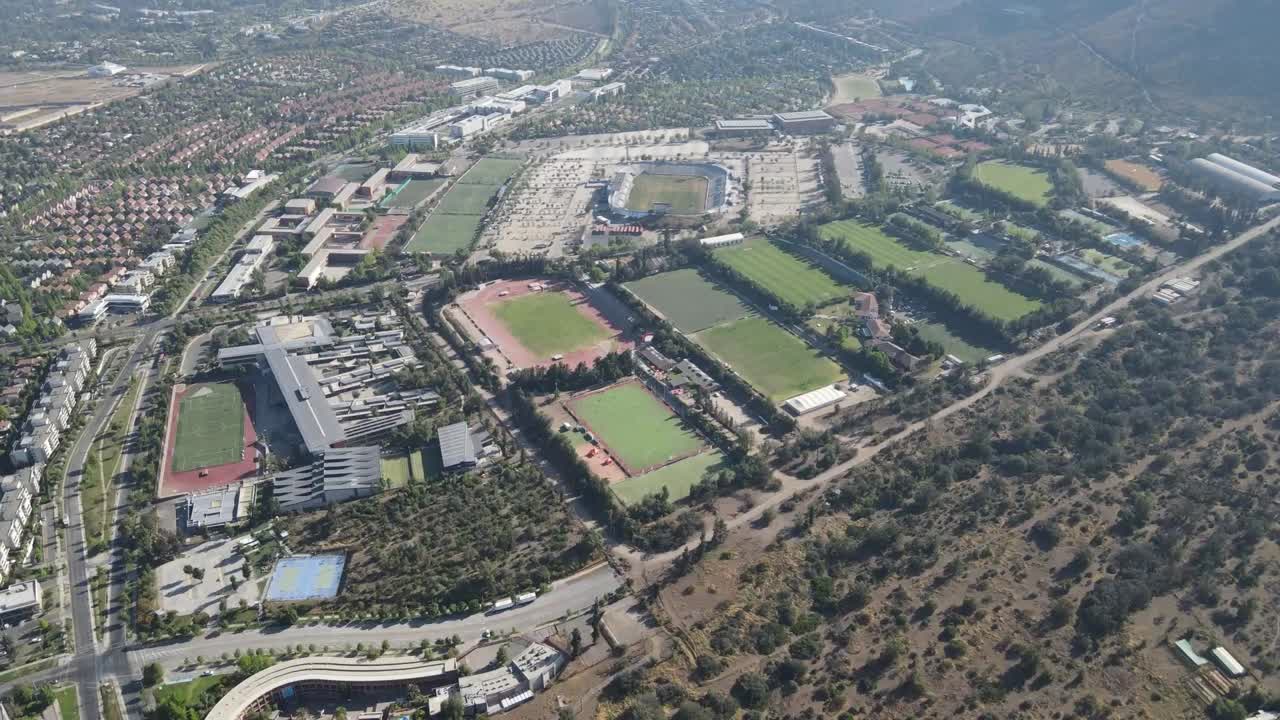 Aerial view panning across a sporting complex with various fields and a stadium, alongside a residential area