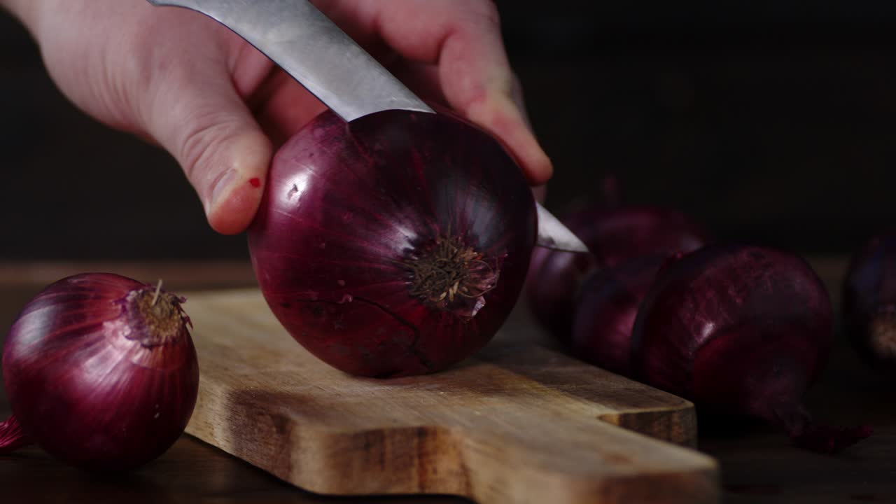 las manos cortan la cebolla roja en dos mitades.