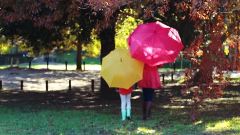 mother and daughter walking together in park under umbrella