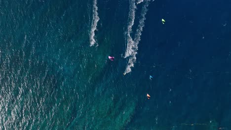 Cuatro-Practicantes-De-Kitesurf-Practicando-Kitesurf-Juntos,-Toma-Aérea-Cinematográfica-De-Gran-Angular-De-Arriba-Hacia-Abajo,-Agua-Azul-Tropical,-Paraíso,-Cámara-Lenta