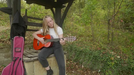 young happy woman musician practices guitar woodland wishing well