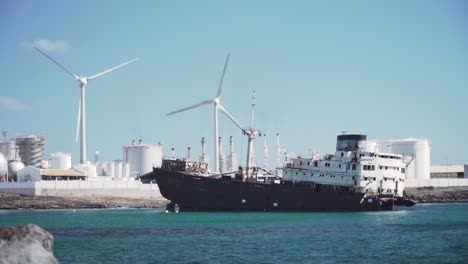 barco abandonado en un puerto industrial costero con turbinas eólicas