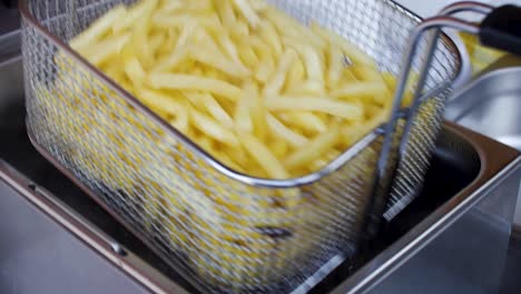mezclar una canasta de alambre de fritura llena de papas fritas y sumergirlas de nuevo en aceite caliente para freírlas
