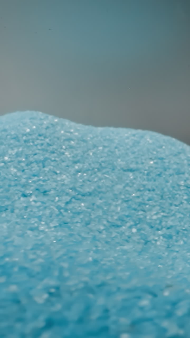 Scattered heap of blue sand shuddering from quakes on light grey background. Bright tiny grains of colored sand shimmering at studio light macro