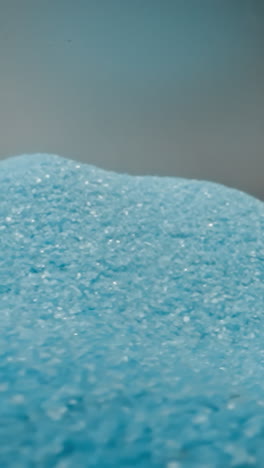 scattered heap of blue sand shuddering from quakes on light grey background. bright tiny grains of colored sand shimmering at studio light macro