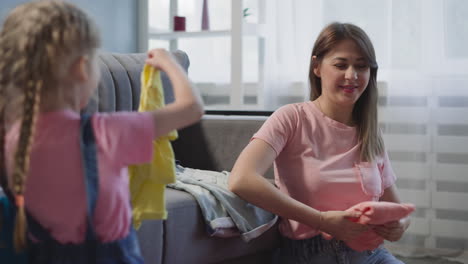 mother folds garment looking at daughter helping with chores