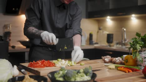 Fresh-green-leek-being-chopped-on-a-wooden-board-by-young-professional-male-chef-in-an-elegant-black-shirt-with-tattoos