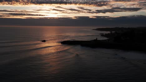 Panning-to-the-left-flyover-of-surfers-at-late-sunset-in-Santa-Cruz,-California