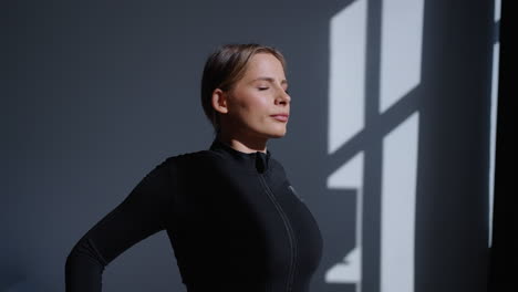 young woman in a black workout shirt standing by a window