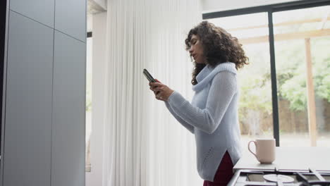 Happy-mature-caucasian-woman-leaning-on-kitchen-counter-using-smartphone-at-home,-slow-motion