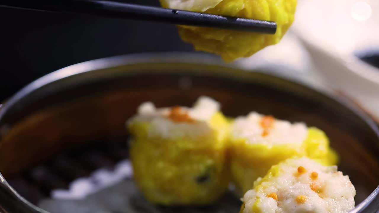 Close-up of chopsticks picking up dumplings from a bamboo steamer, highlighting texture and detail.