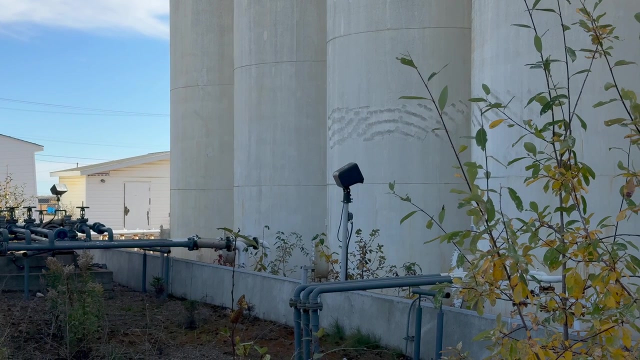 Una panoramica su un deposito di petrolio abbandonato, che mostra serbatoi arrugginiti e strutture logore in un contesto semi-rurale