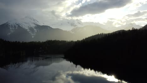 beautiful drone shot of a lake with mountains in the background with sun showers and rain onto the lake - shot taken in squamish, bc