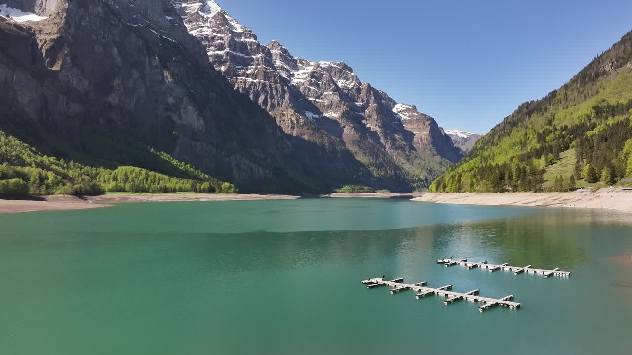 Peaceful view of turquoise Klöntalersee lake with floating docks and snow capped Alps in Glarus Switzerland