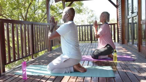 Focused-senior-african-american-couple-practicing-yoga-on-mats-on-sunny-terrace,-slow-motion