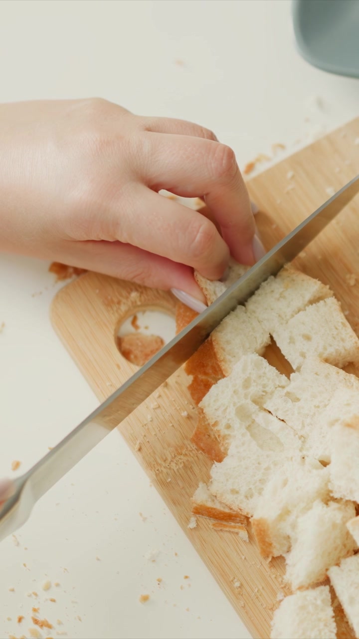 Woman hands carefully cut loaf of bread into small pieces on wooden cutting board. fresh white bread is sliced with precision and soft texture details are visible throughout process. clean