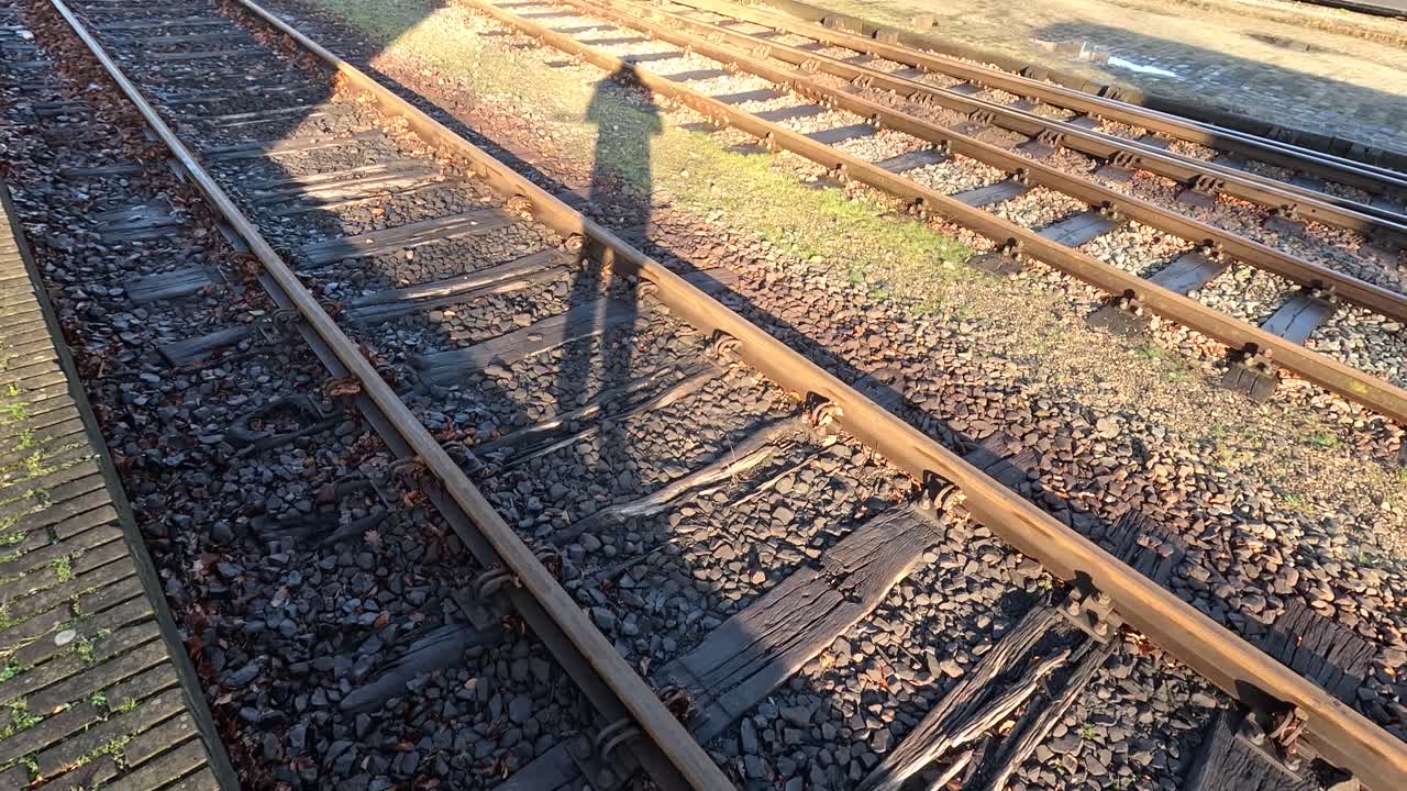 A shadow of a man standing at the train tracks, the sun is low and the train station is old and weathered.